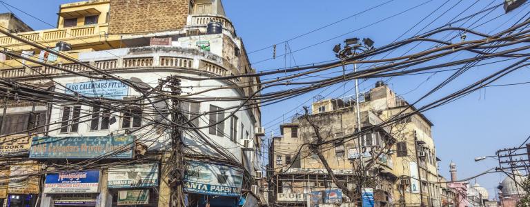 Crowded market street in Old Dehli with a mess of power lines overhead.