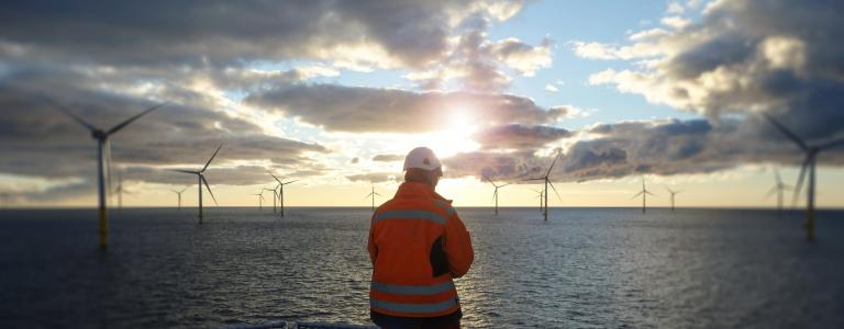 A worker looks out at offshore wind turbines at sunset.
